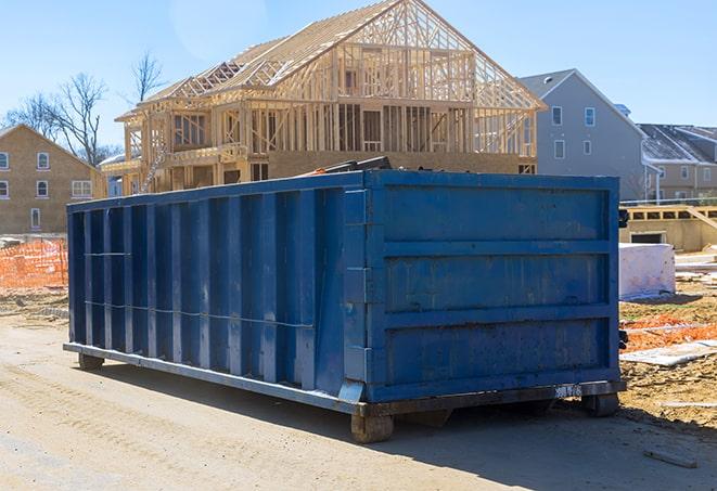 a line of rectangular dumpsters standing in a driveway near a detached garage